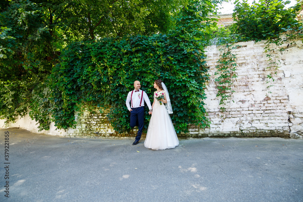 man groom in a white shirt and trousers, a beautiful bride in a white dress and veil, posing and walking along the street on a wedding day