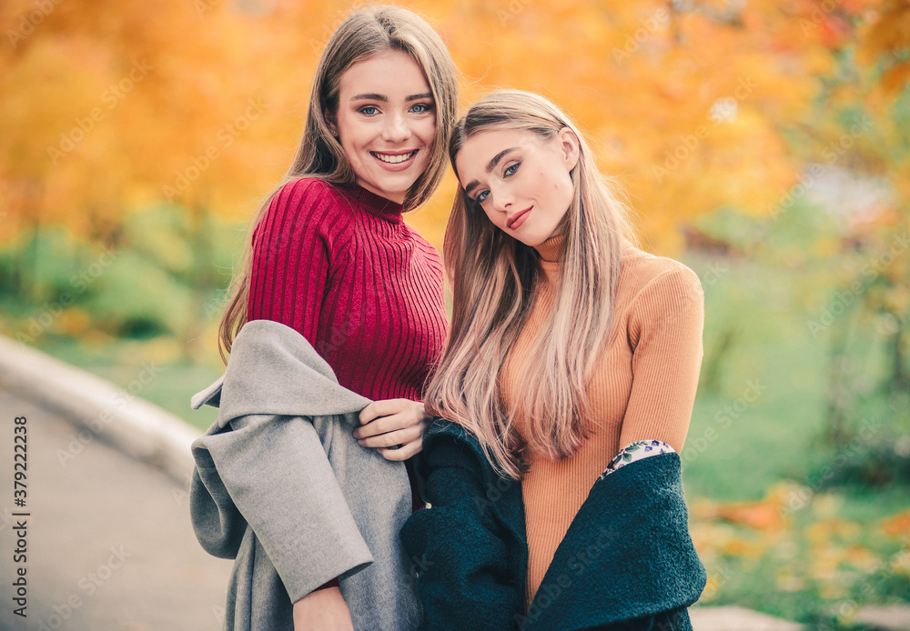 Fototapeta premium Two young beautiful smiling women in autumn clothes on a background of yellow foliage.