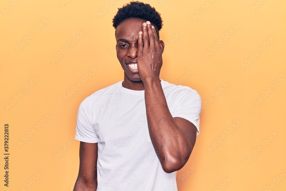 Young african american man wearing casual clothes covering one eye with hand, confident smile on face and surprise emotion. Young african american man wearing casual clothes covering one eye with hand, confident smile on face and surprise emotion.