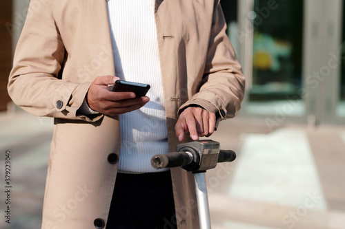 Businessman scrolling in smartphone while touching panel on electric scooter