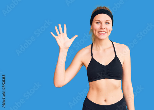 Young beautiful blonde woman wearing sportswear showing and pointing up with fingers number five while smiling confident and happy. © Krakenimages.com