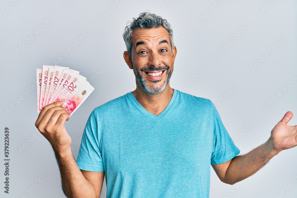 Middle age grey-haired man holding israel shekels celebrating achievement with happy smile and winner expression with raised hand Middle age grey-haired man holding israel shekels celebrating achievement with happy smile and winner expression with raised hand