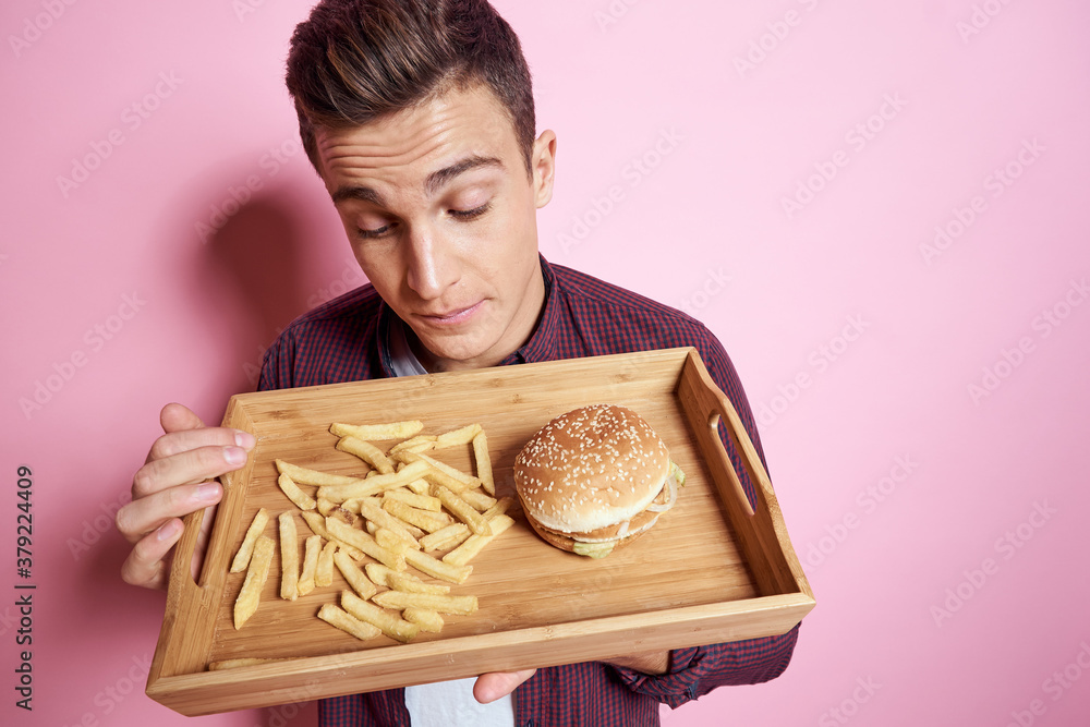 Man with fast food eating hamburger french fries pink background Man with fast food eating hamburger french fries pink background