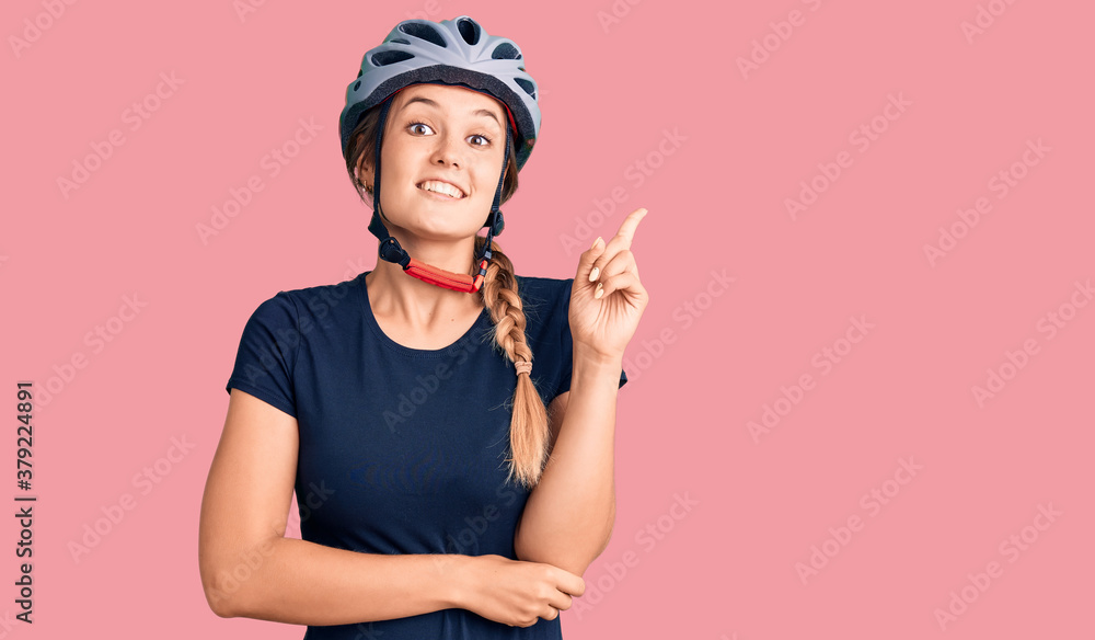 Beautiful caucasian woman wearing bike helmet with a big smile on face, pointing with hand and finger to the side looking at the camera. Beautiful caucasian woman wearing bike helmet with a big smile on face, pointing with hand and finger to the side looking at the camera.