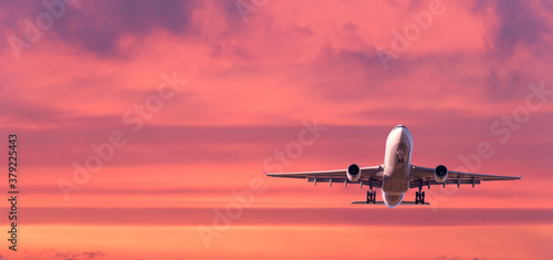 Airplane is flying in colorful sky at sunset. Landscape with white passenger airplane, purple sky with pink clouds. Aircraft takes off. Business trip. Commercial plane. Travel. Aerial view. Concept © den-belitsky