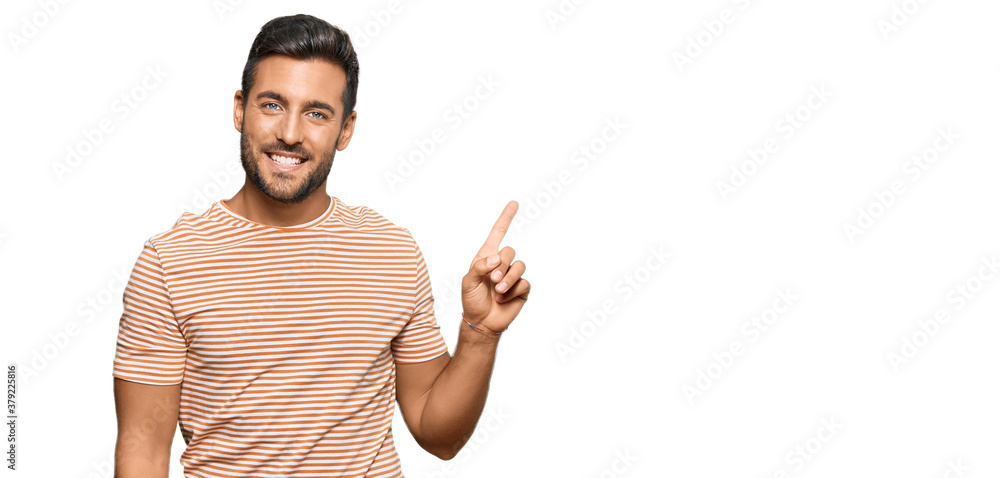 Handsome hispanic man wearing casual clothes with a big smile on face, pointing with hand finger to the side looking at the camera. Handsome hispanic man wearing casual clothes with a big smile on face, pointing with hand finger to the side looking at the camera.