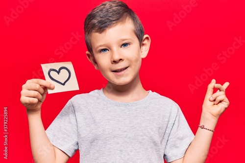 Cute blond kid holding heart reminder smiling happy pointing with hand and finger to the side © Krakenimages.com