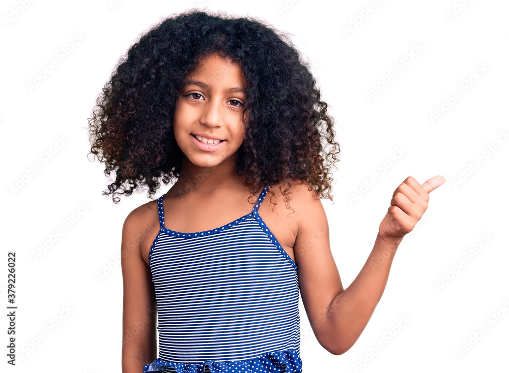 African american child with curly hair wearing swimwear smiling with happy face looking and pointing to the side with thumb up. African american child with curly hair wearing swimwear smiling with happy face looking and pointing to the side with thumb up.