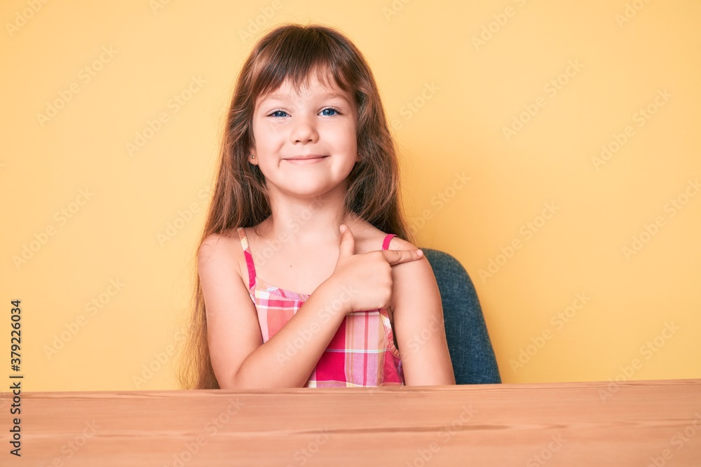 Little caucasian kid girl with long hair wearing casual clothes sitting on the table smiling cheerful pointing with hand and finger up to the side Little caucasian kid girl with long hair wearing casual clothes sitting on the table smiling cheerful pointing with hand and finger up to the side