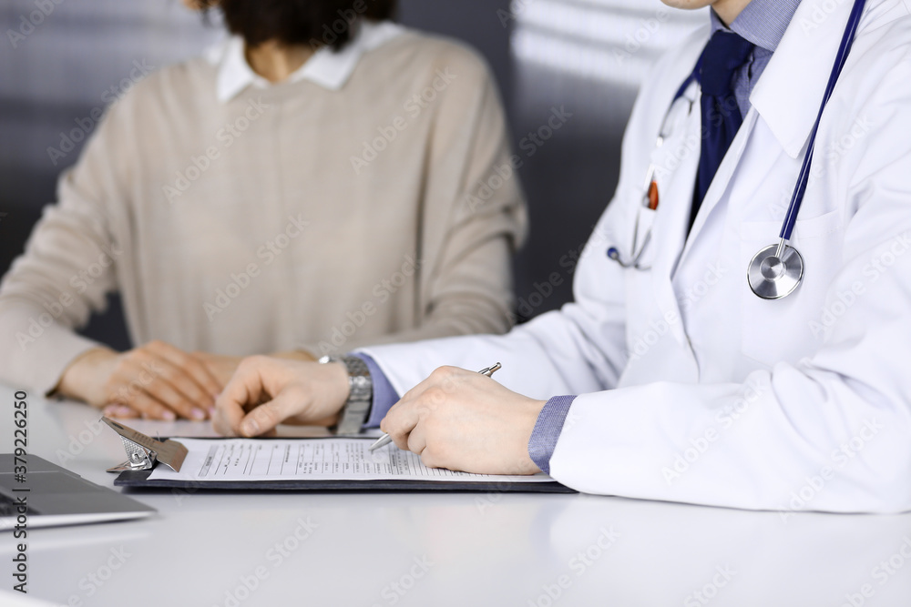 Unknown male doctor and patient woman discussing something while sitting in clinic and using clipboard. Best medical service in hospital, medicine, pandemic stop Unknown male doctor and patient woman discussing something while sitting in clinic and using clipboard. Best medical service in hospital, medicine, pandemic stop