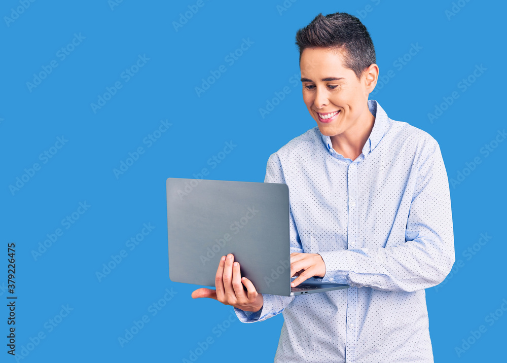 Young woman with short hair holding laptop looking positive and happy standing and smiling with a confident smile showing teeth Young woman with short hair holding laptop looking positive and happy standing and smiling with a confident smile showing teeth