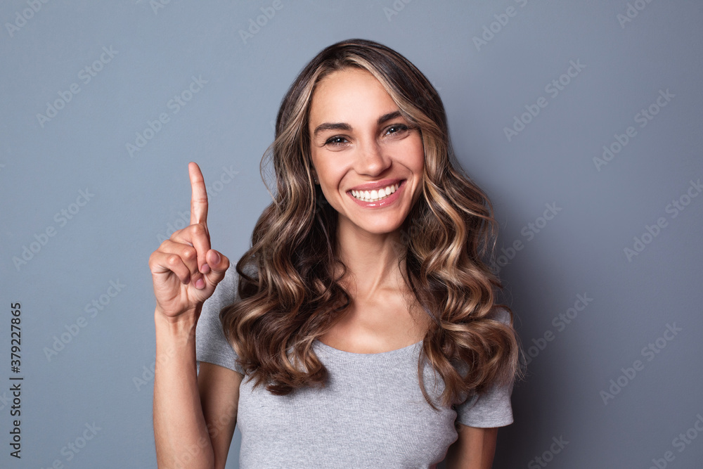 Happy smiling caucasian woman points up while posing over gray wall. Female portrait. Happy smiling caucasian woman points up while posing over gray wall. Female portrait.