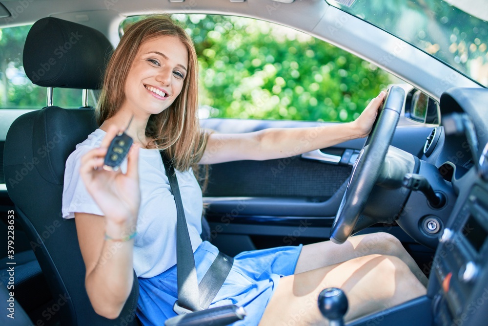 Young beautiful blonde woman smiling happy sitting at the car showing key Young beautiful blonde woman smiling happy sitting at the car showing key