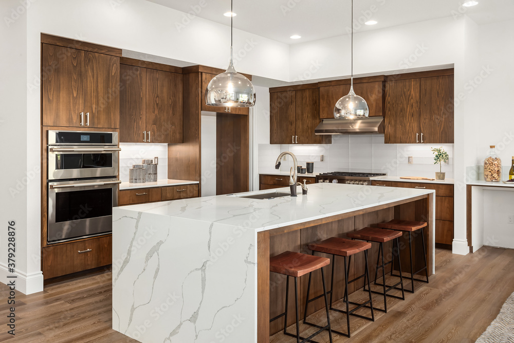 Kitchen in new luxury home with quartz waterfall island, hardwood floors, dark wood cabinets, and stainless steel appliances. - obrazy, fototapety, plakaty 
