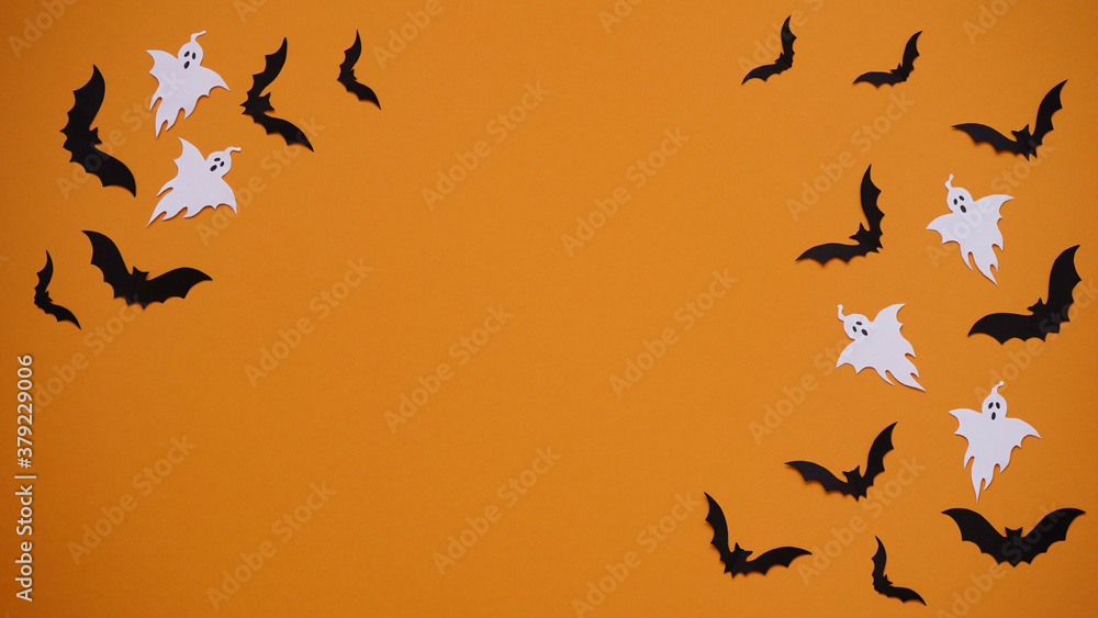 Halloween holiday concept. Black paper bats and ghosts on bright orange background, top view, flat lay,copy spaes.Celebration of the dead