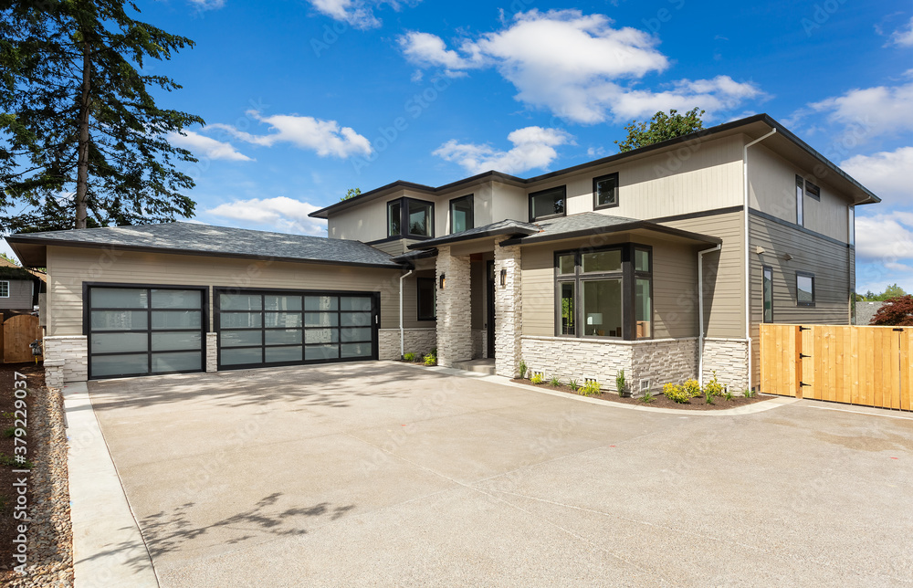 Beautiful modern home exterior with three car garage and large driveway. Backdrop of blue sky and clouds.