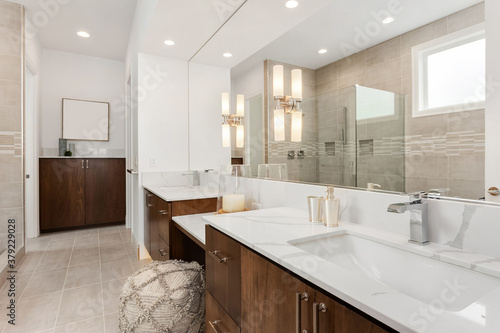 Beautiful bathroom in new luxury home with double vanity and two large sinks. Mirror reflection shows walk in shower.
