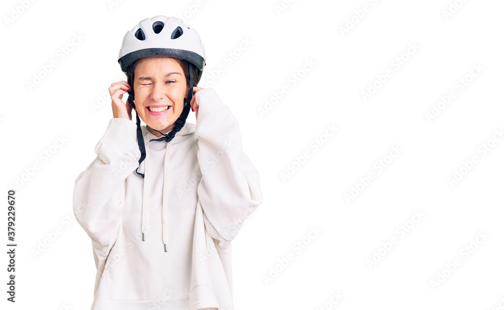 Beautiful brunette young woman wearing bike helmet and sporty clothes covering ears with fingers with annoyed expression for the noise of loud music. deaf concept. Beautiful brunette young woman wearing bike helmet and sporty clothes covering ears with fingers with annoyed expression for the noise of loud music. deaf concept.