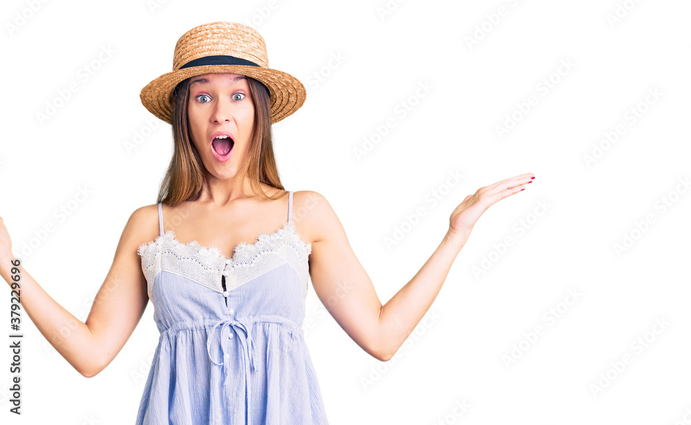 Beautiful brunette young woman wearing summer hat celebrating victory with happy smile and winner expression with raised hands Beautiful brunette young woman wearing summer hat celebrating victory with happy smile and winner expression with raised hands