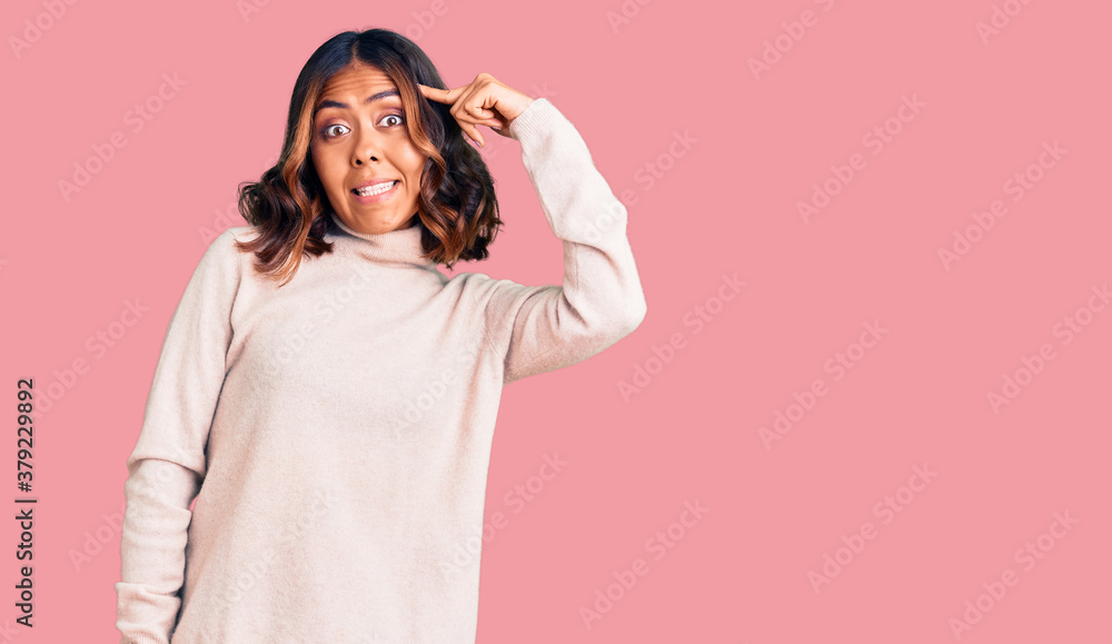 Young beautiful mixed race woman wearing winter turtleneck sweater smiling pointing to head with one finger, great idea or thought, good memory Young beautiful mixed race woman wearing winter turtleneck sweater smiling pointing to head with one finger, great idea or thought, good memory