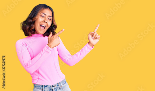 Young beautiful mixed race woman wearing pink shirt smiling and looking at the camera pointing with two hands and fingers to the side.