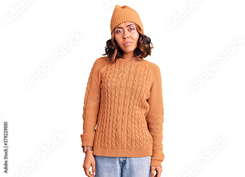 Young beautiful mixed race woman wearing wool sweater and winter hat relaxed with serious expression on face. simple and natural looking at the camera. photo