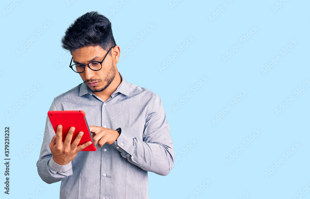 Handsome latin american young man holding touchpad thinking attitude and sober expression looking self confident Handsome latin american young man holding touchpad thinking attitude and sober expression looking self confident