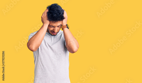 Handsome latin american young man wearing casual tshirt suffering from headache desperate and stressed because pain and migraine. hands on head.