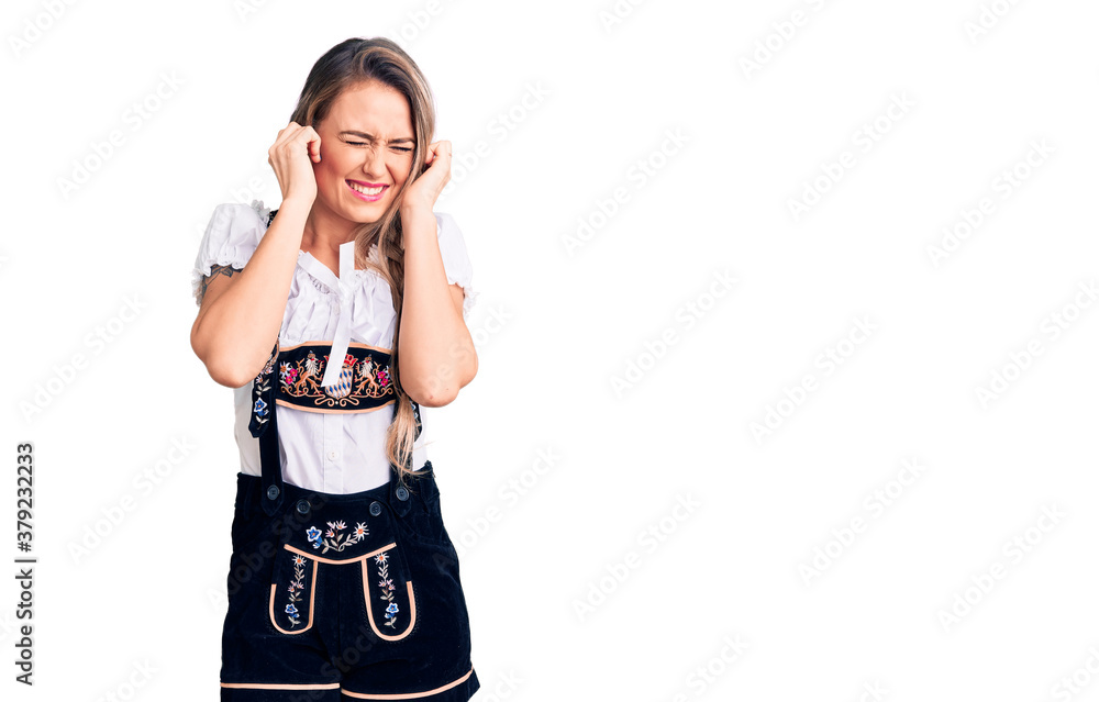 Young beautiful blonde woman wearing oktoberfest dress covering ears with fingers with annoyed expression for the noise of loud music. deaf concept. Young beautiful blonde woman wearing oktoberfest dress covering ears with fingers with annoyed expression for the noise of loud music. deaf concept.