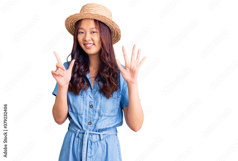 Young beautiful chinese girl wearing summer hat showing and pointing up with fingers number seven while smiling confident and happy. Young beautiful chinese girl wearing summer hat showing and pointing up with fingers number seven while smiling confident and happy.