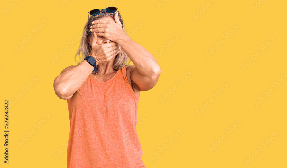 Middle age fit blonde woman wearing casual summer clothes and sunglasses covering eyes and mouth with hands, surprised and shocked. hiding emotion Middle age fit blonde woman wearing casual summer clothes and sunglasses covering eyes and mouth with hands, surprised and shocked. hiding emotion
