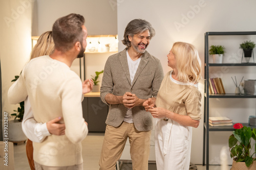 Two cheerful couples in casualwear discussing latest news in living-room