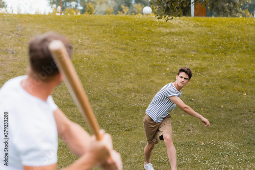 Sticker selective focus of teenager boy throwing ball while playing baseball with father