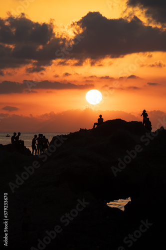 Sunset silhouettes. Groups of young people looking at the sunset from a rock in the sea on the coast of Tropea, Calabria. italian summer and vacation mood, amazing colored sunset sky, reflections.