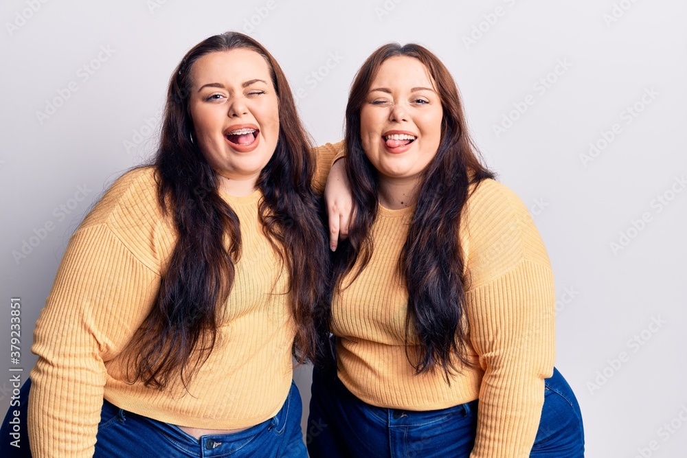 Young plus size twins wearing casual clothes winking looking at the camera with sexy expression, cheerful and happy face. Young plus size twins wearing casual clothes winking looking at the camera with sexy expression, cheerful and happy face.