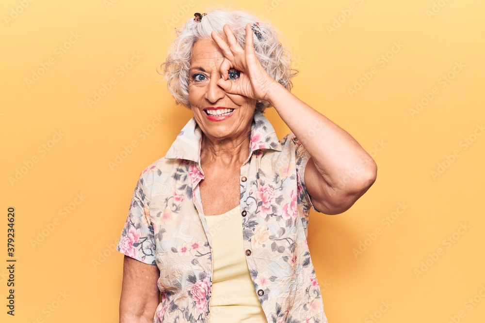 Senior grey-haired woman wearing casual clothes smiling happy doing ok sign with hand on eye looking through fingers Senior grey-haired woman wearing casual clothes smiling happy doing ok sign with hand on eye looking through fingers