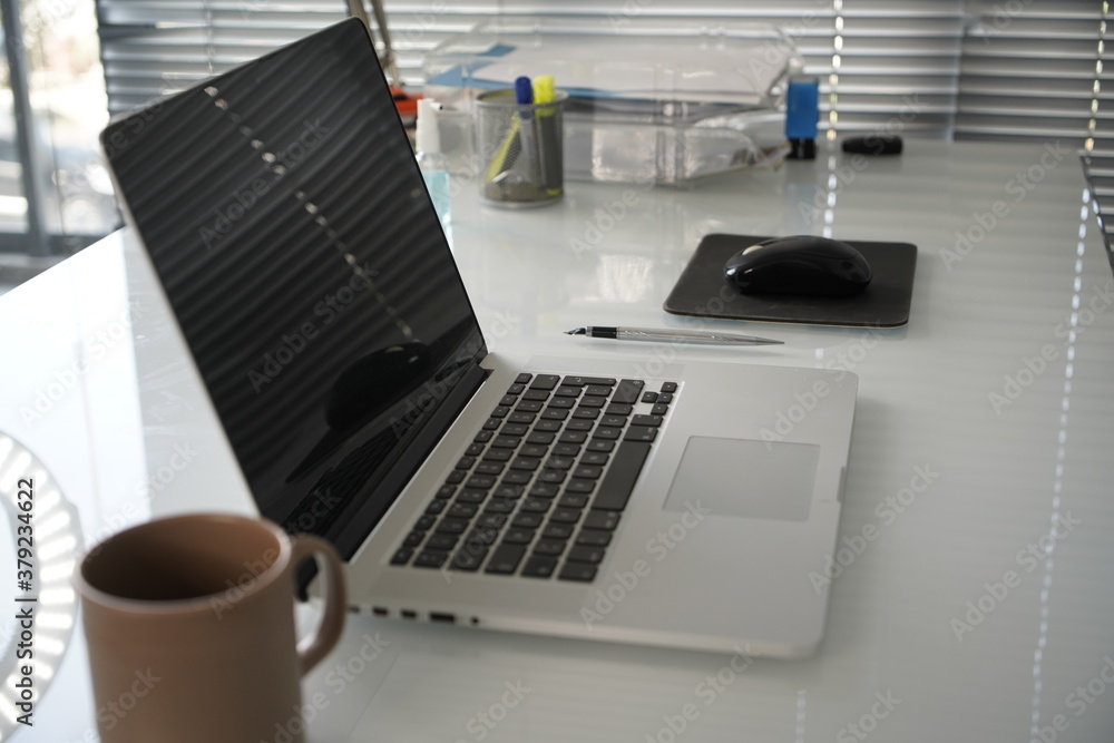 Close up view of simple workspace with laptop, smartphone, coffee cup and tree pot on white table with blurred office room background. Close up view of simple workspace with laptop, smartphone, coffee cup and tree pot on white table with blurred office room background.