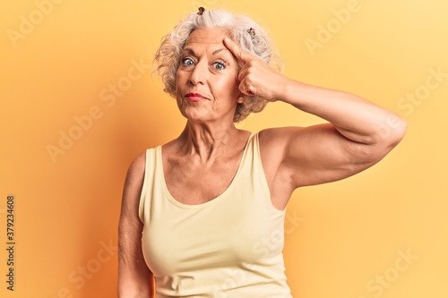 Senior grey-haired woman wearing casual clothes pointing unhappy to pimple on forehead, ugly infection of blackhead. acne and skin problem