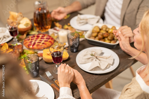 Hands of family members saying thanks to Lord while praying by festive table