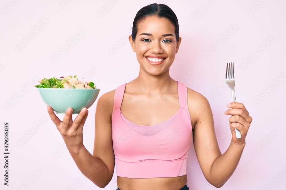Young beautiful latin girl wearing sportswear holding salad smiling with a happy and cool smile on face. showing teeth. Young beautiful latin girl wearing sportswear holding salad smiling with a happy and cool smile on face. showing teeth.