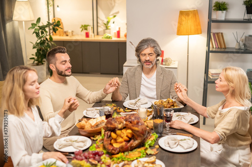 Two couples in casualwear keeping eyes closed while sitting by festive table
