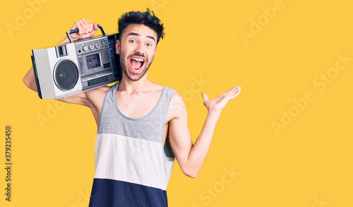 Young hispanic man holding boombox, listening to music celebrating victory with happy smile and winner expression with raised hands