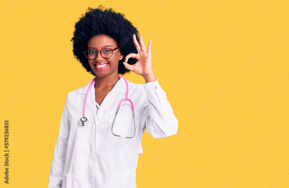 Young african american woman wearing doctor coat and stethoscope smiling positive doing ok sign with hand and fingers. successful expression. Young african american woman wearing doctor coat and stethoscope smiling positive doing ok sign with hand and fingers. successful expression.