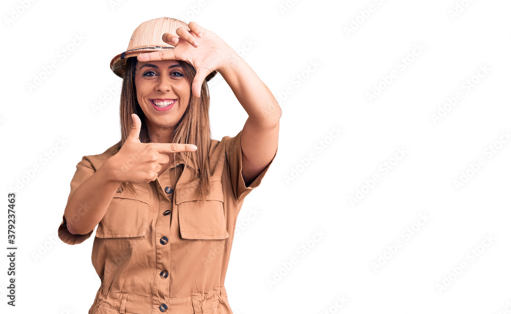 Fototapeta premium Young beautiful woman wearing explorer hat smiling making frame with hands and fingers with happy face. creativity and photography concept.