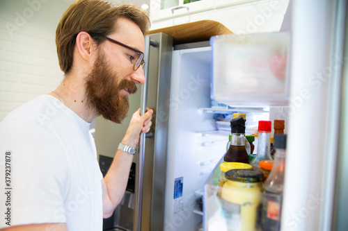 Young man looking into an open home fridge, a refrigerator.