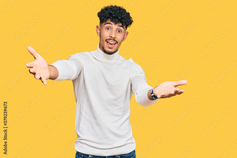Young arab man wearing casual winter sweater looking at the camera smiling with open arms for hug. cheerful expression embracing happiness. Young arab man wearing casual winter sweater looking at the camera smiling with open arms for hug. cheerful expression embracing happiness.