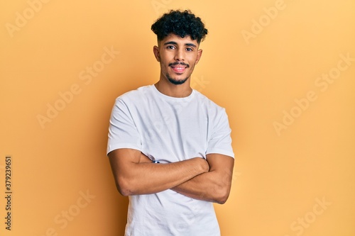 Young arab handsome man wearing casual white tshirt happy face smiling with crossed arms looking at the camera. positive person.