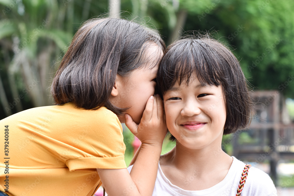 Two little sister girls whisper in ear at park outdoor. Two little sister girls whisper in ear at park outdoor.
