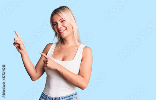 Foto Young beautiful blonde woman wearing casual sleeveless t-shirt smiling and looking at the camera pointing with two hands and fingers to the side