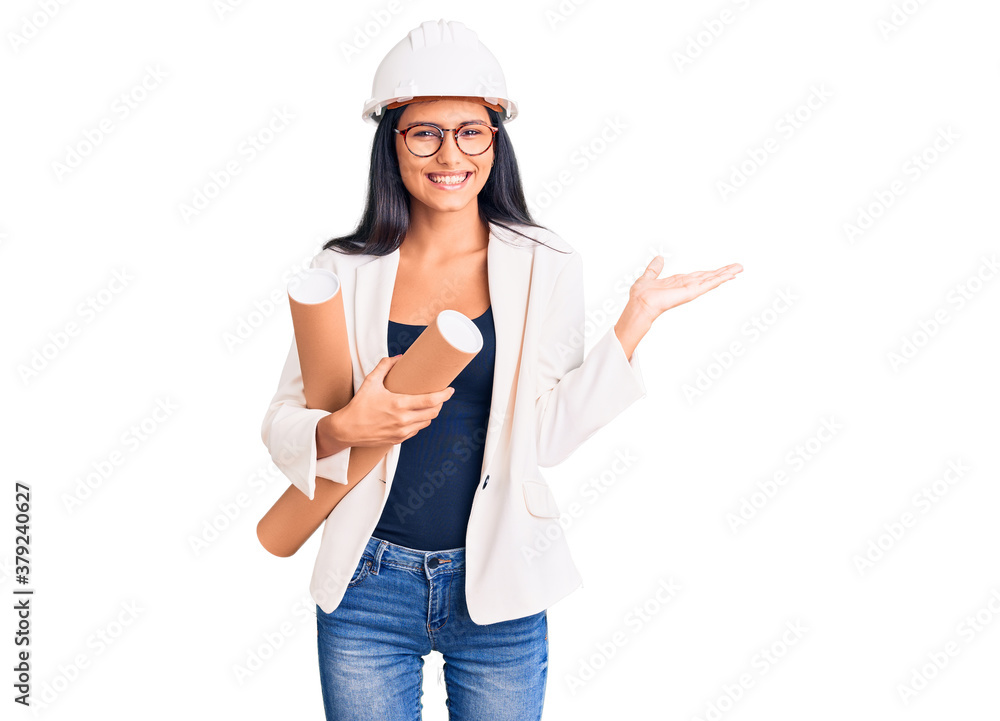 Young beautiful latin girl wearing architect hardhat holding blueprints celebrating victory with happy smile and winner expression with raised hands Young beautiful latin girl wearing architect hardhat holding blueprints celebrating victory with happy smile and winner expression with raised hands